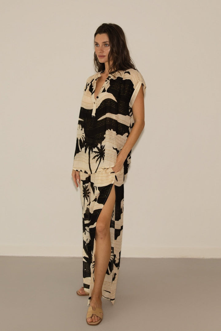 Woman wearing a black and white patterned outfit with a slit skirt on a plain background