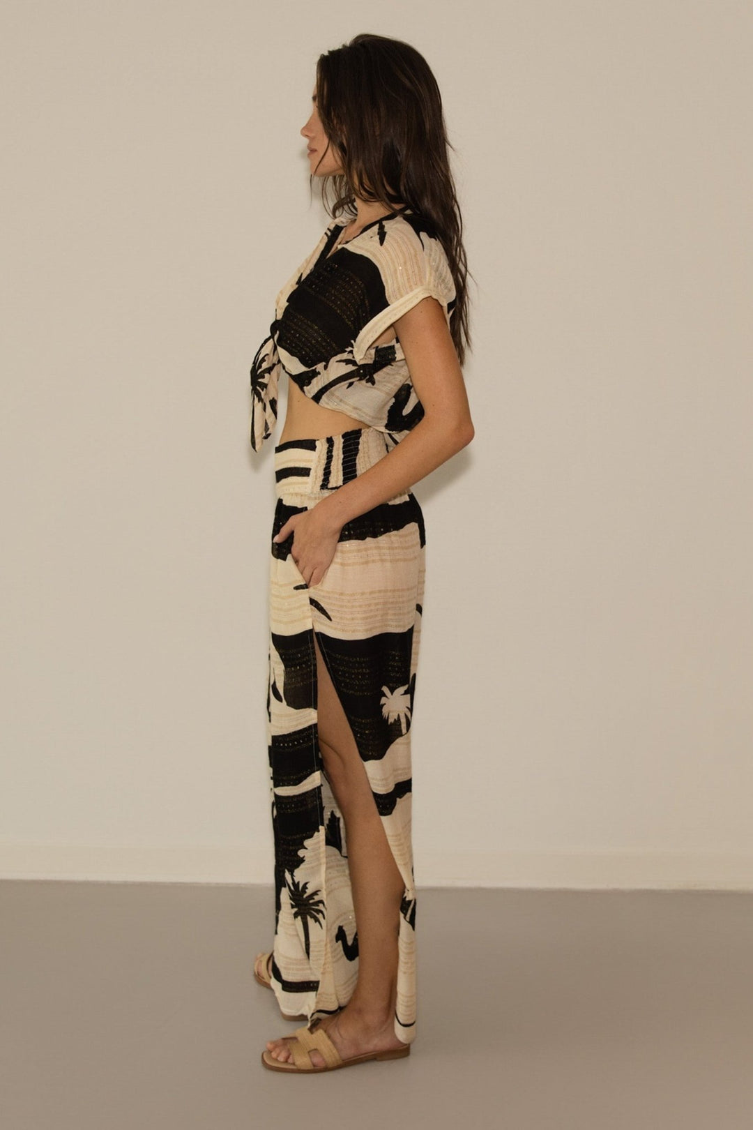 Woman wearing a black and beige patterned dress with a slit on a plain background