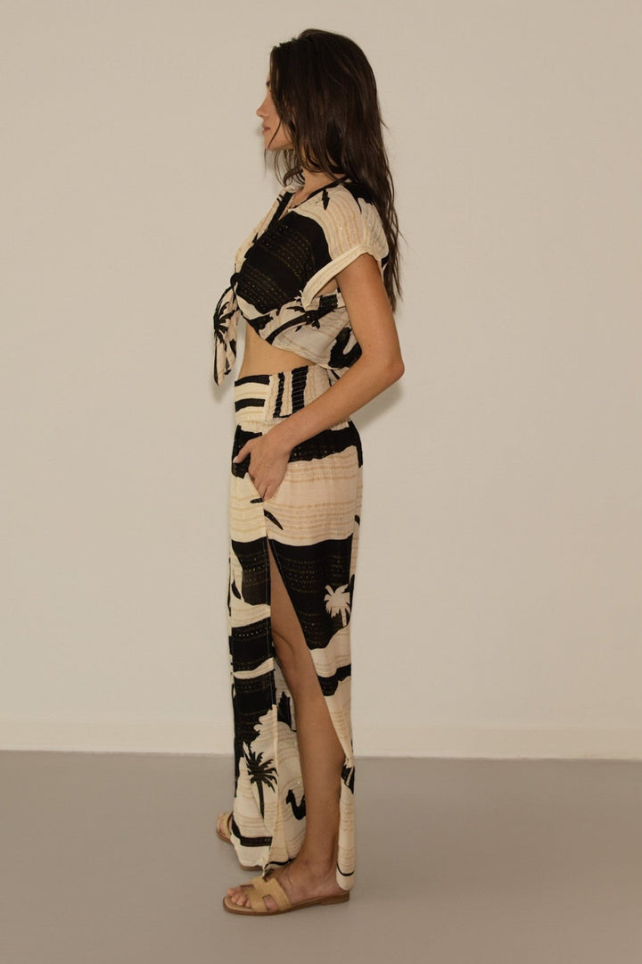 Woman wearing a black and beige patterned dress with a slit on a plain background