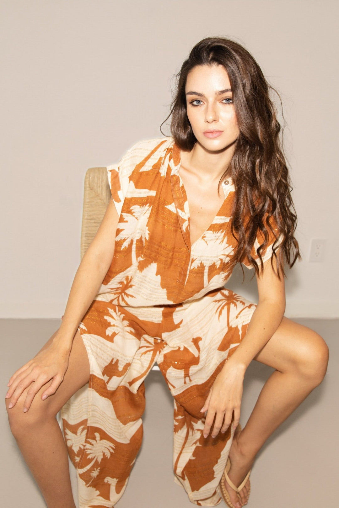 Woman wearing a brown and beige floral jumpsuit sitting on a chair.