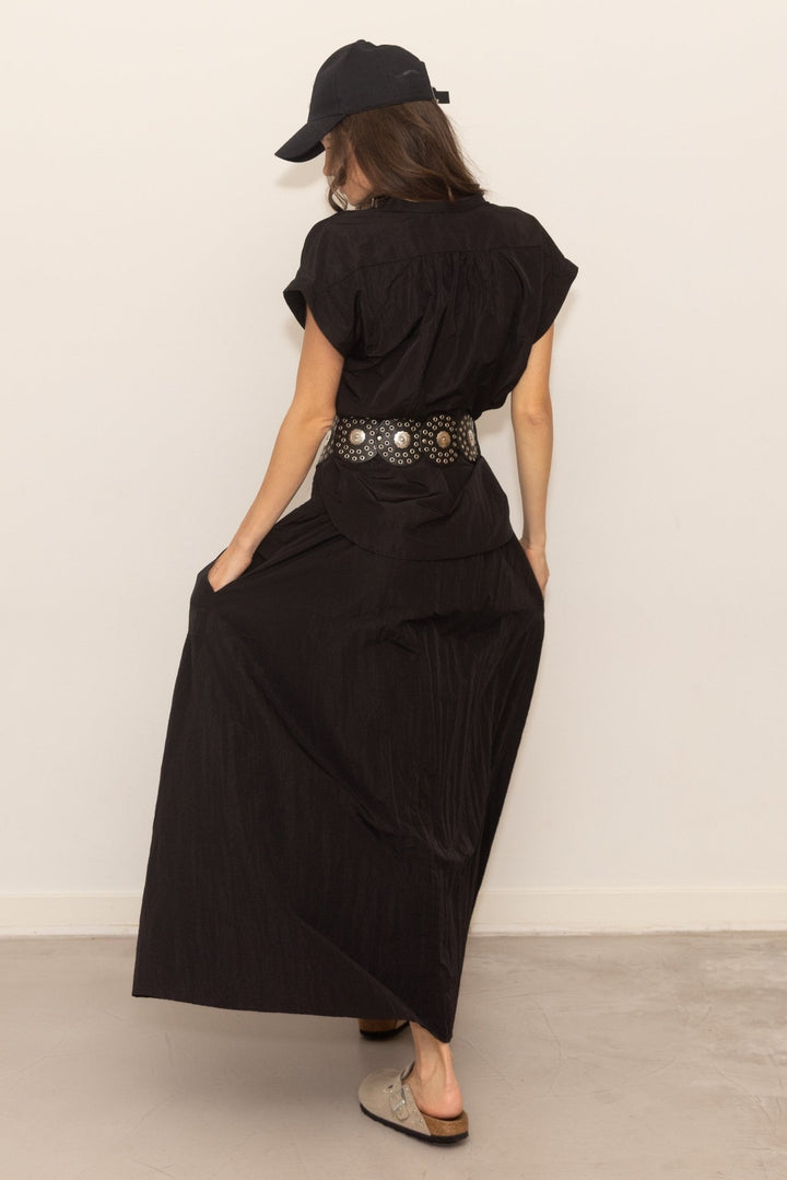 Person wearing a black outfit with a belt and cap against a plain background