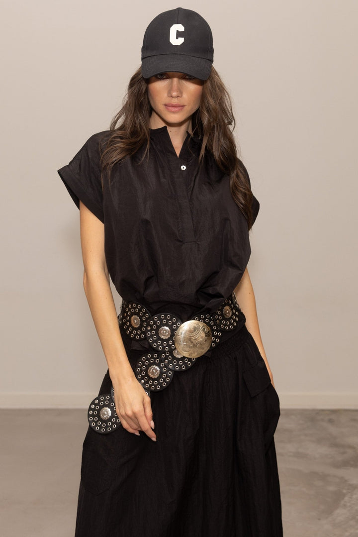 Woman wearing a black outfit with a decorative belt and cap against a plain background