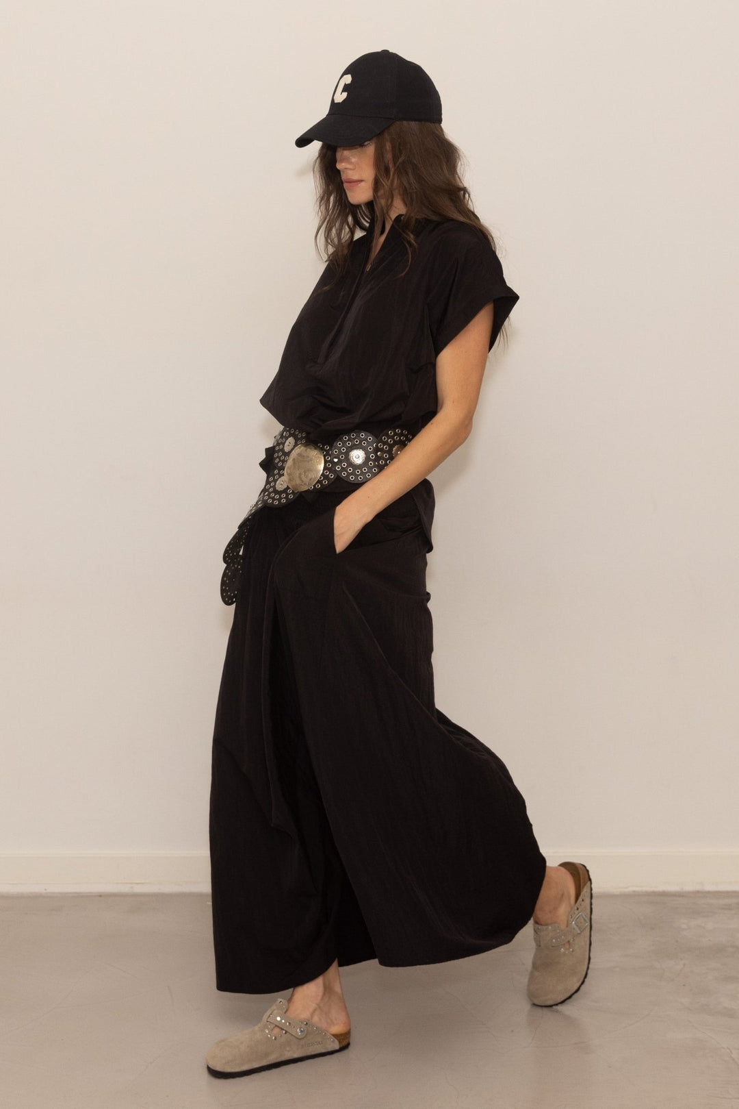 Person wearing a black outfit with wide-leg pants and a cap against a white background