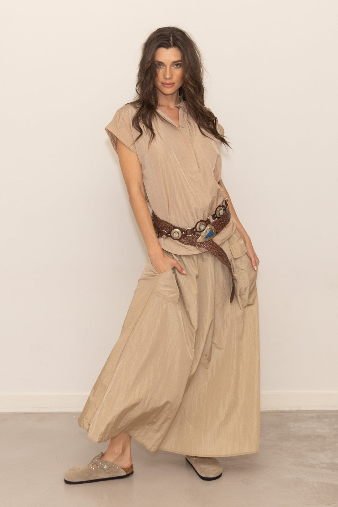 Woman wearing a beige outfit with a belt against a white background