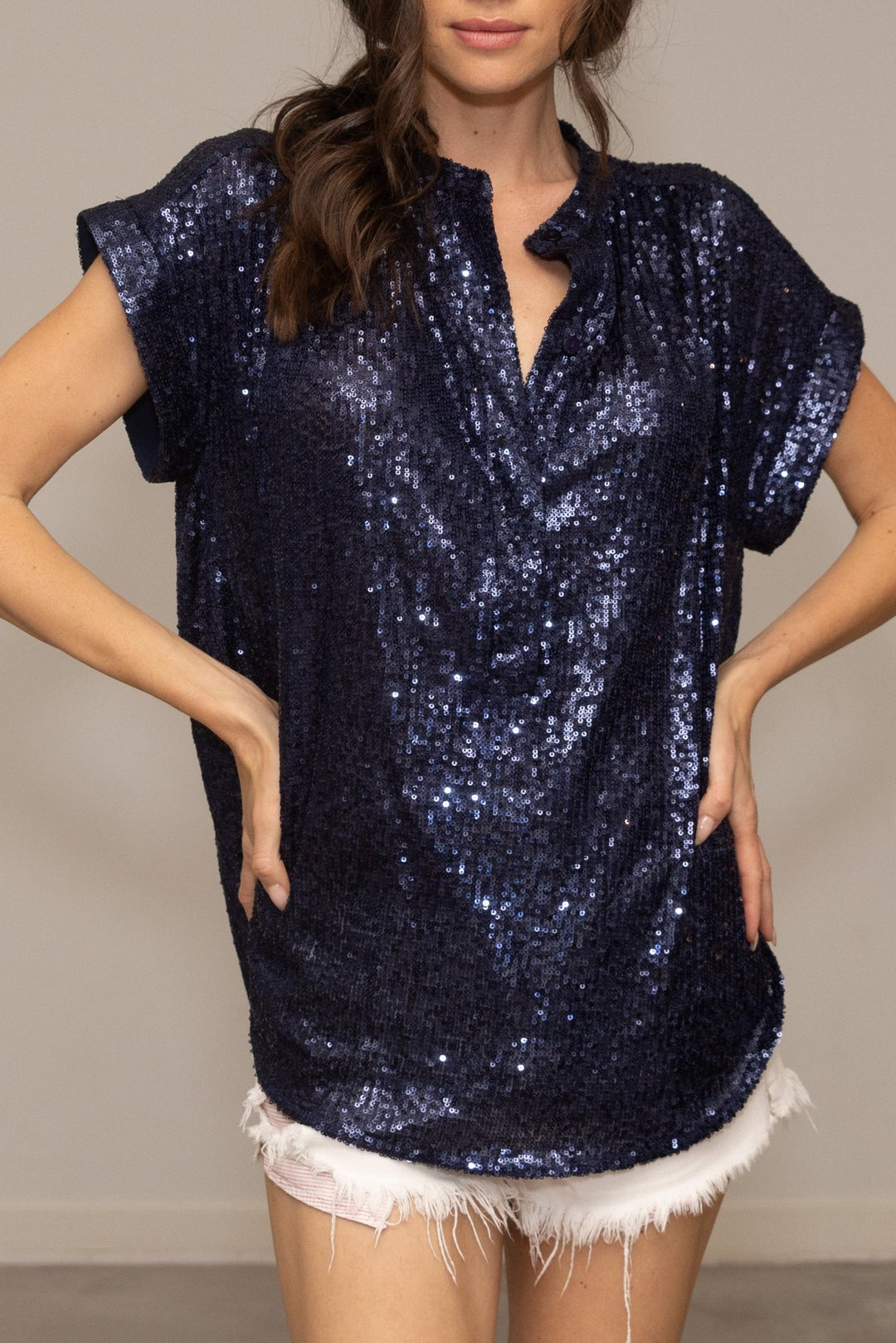 Woman wearing a navy sequin top and white shorts against a neutral background