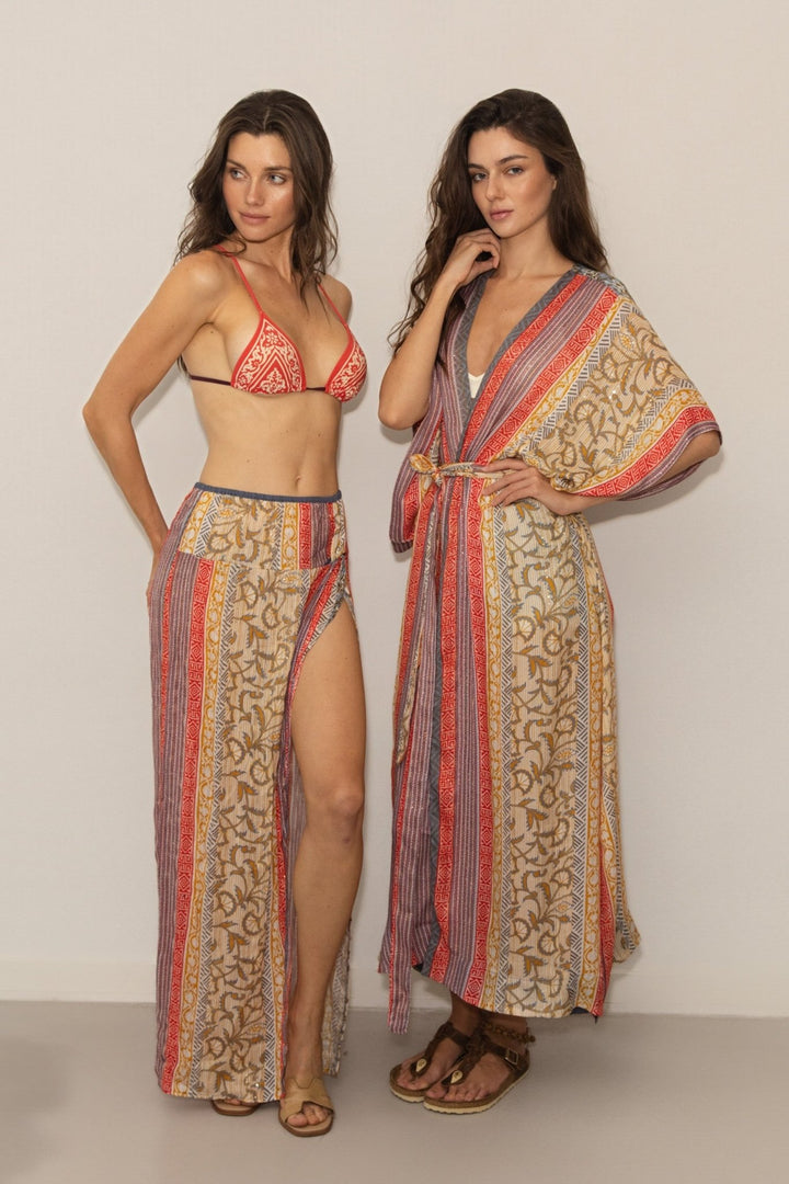 Two women wearing patterned swimsuit and cover-up on a plain background