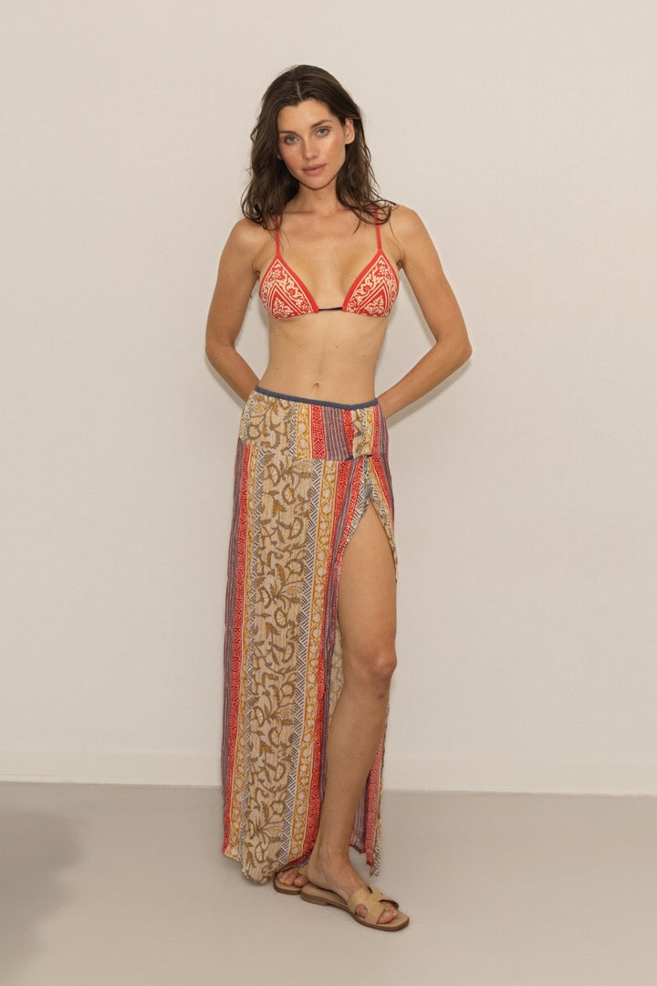 Woman wearing a patterned bikini and long skirt against a plain background
