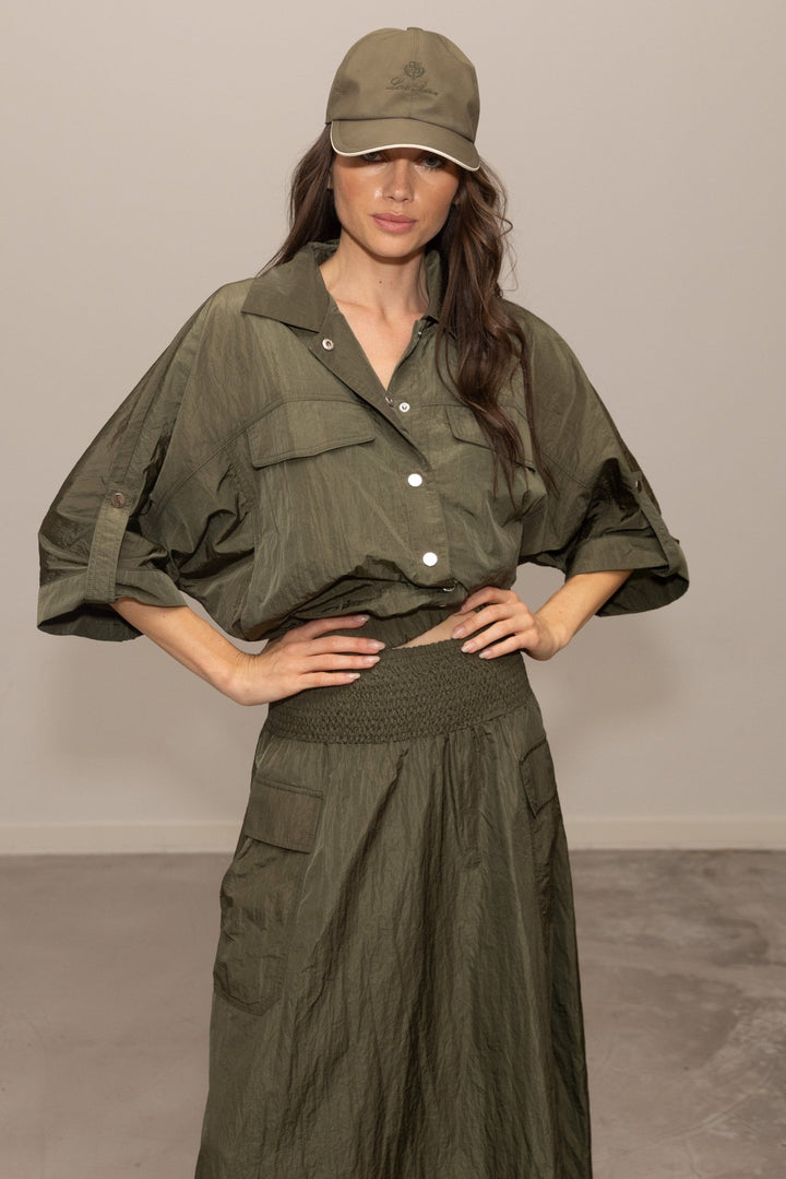 Person wearing an olive green outfit with a matching cap against a plain background
