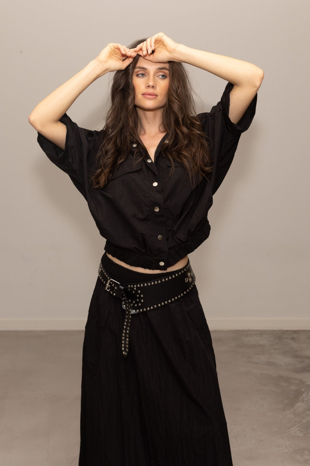 Woman wearing a black outfit with a studded belt against a plain background