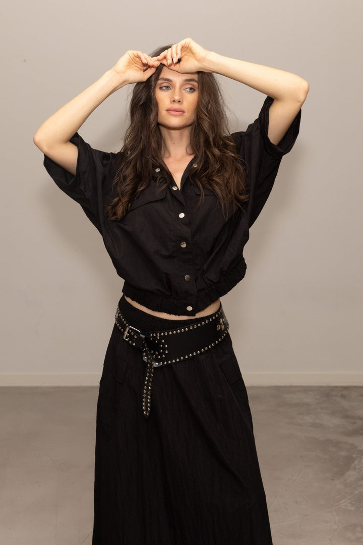 Woman wearing a black outfit with a studded belt against a plain background