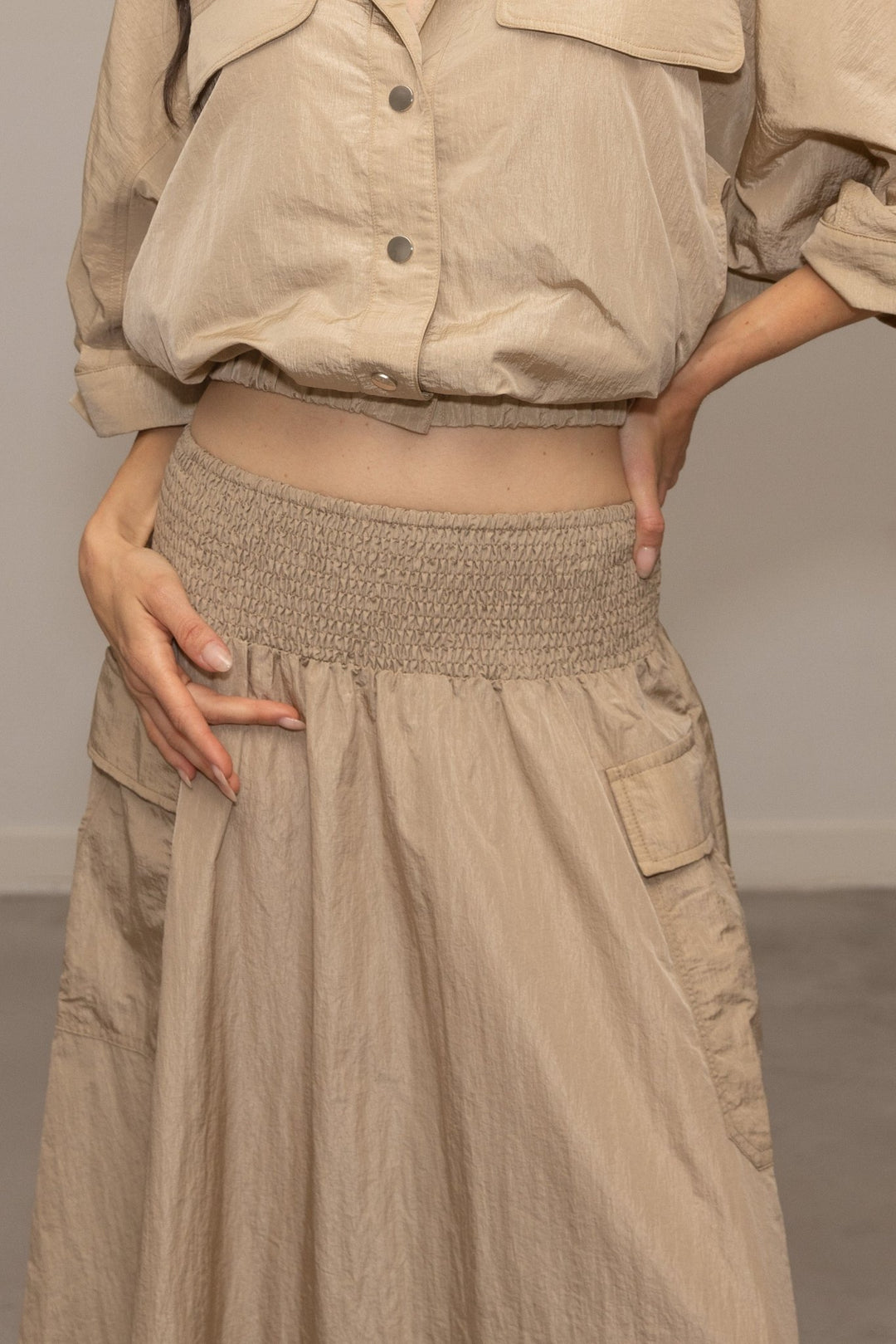 Person wearing a beige outfit with a skirt and jacket against a neutral background
