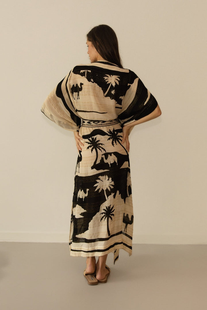 Woman wearing a patterned dress with desert-themed design on a plain background