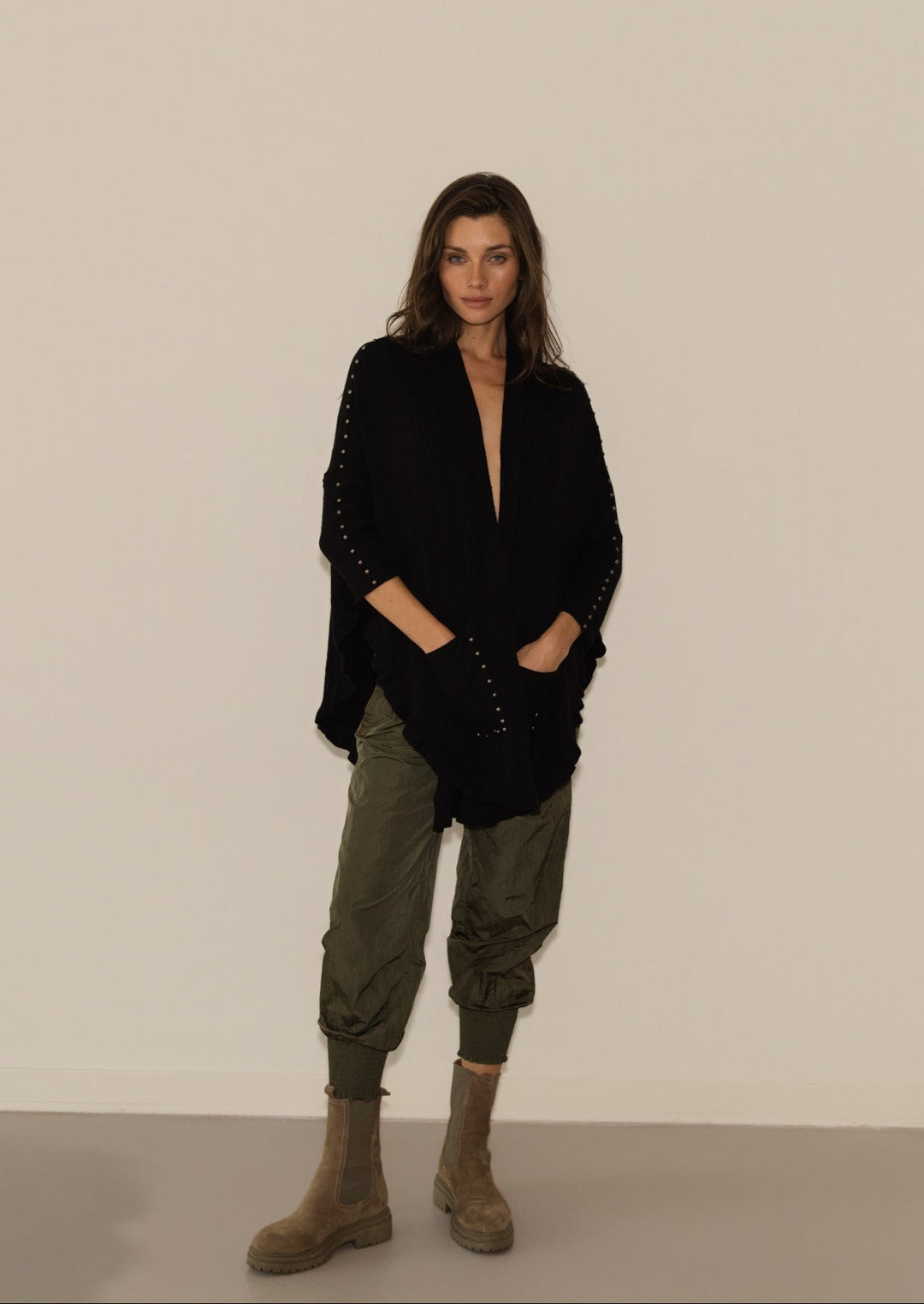 Woman wearing a black jacket and green pants standing against a plain background