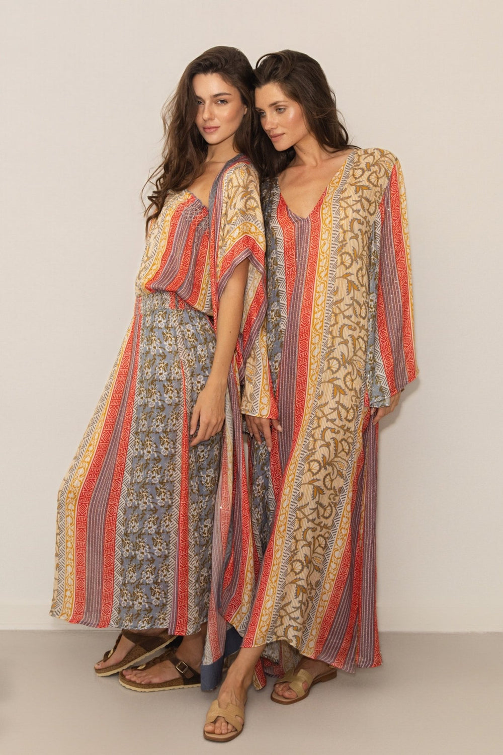 Two women wearing patterned kaftans against a plain background