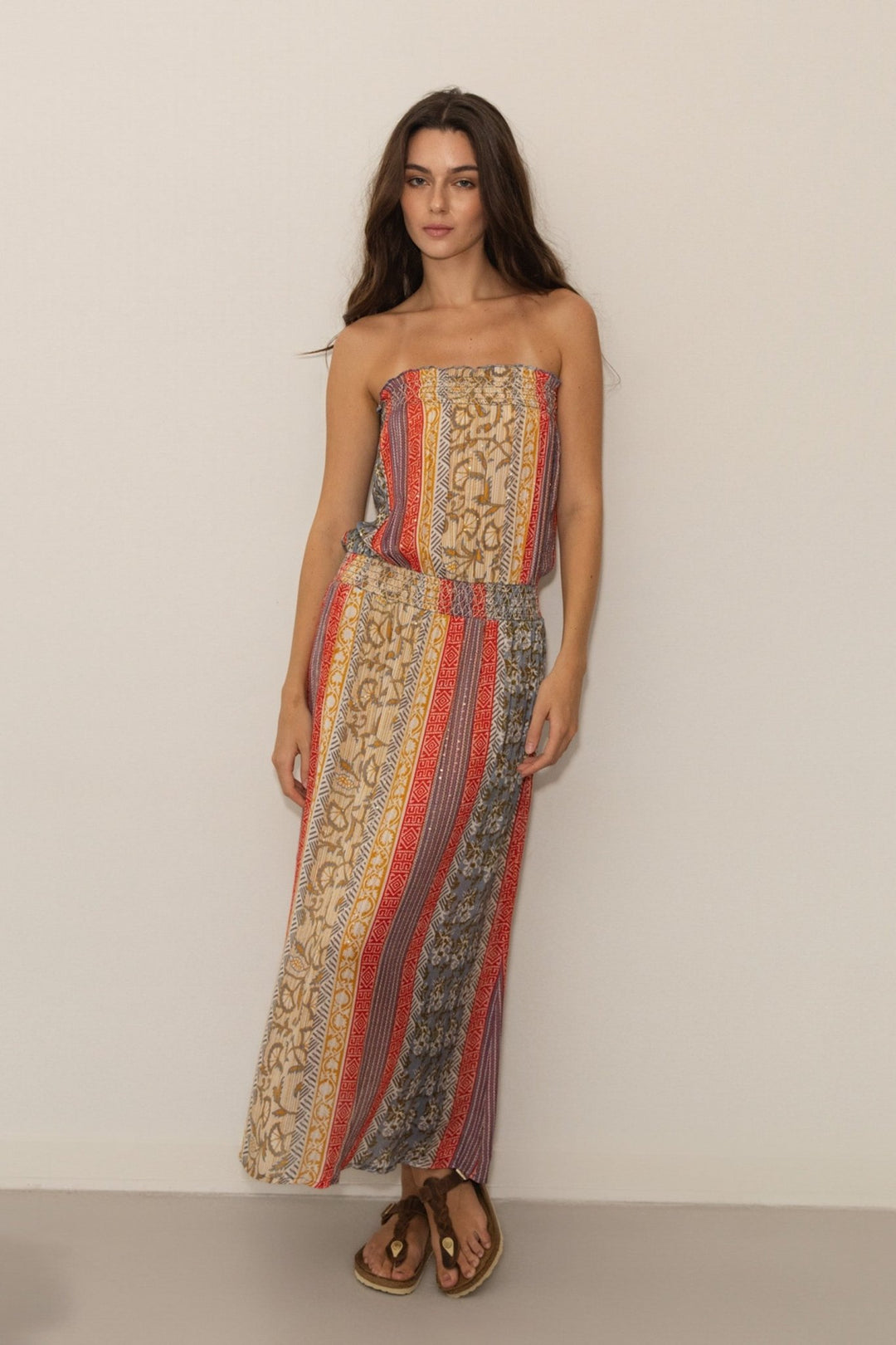 Woman wearing a strapless, long, patterned dress against a plain background