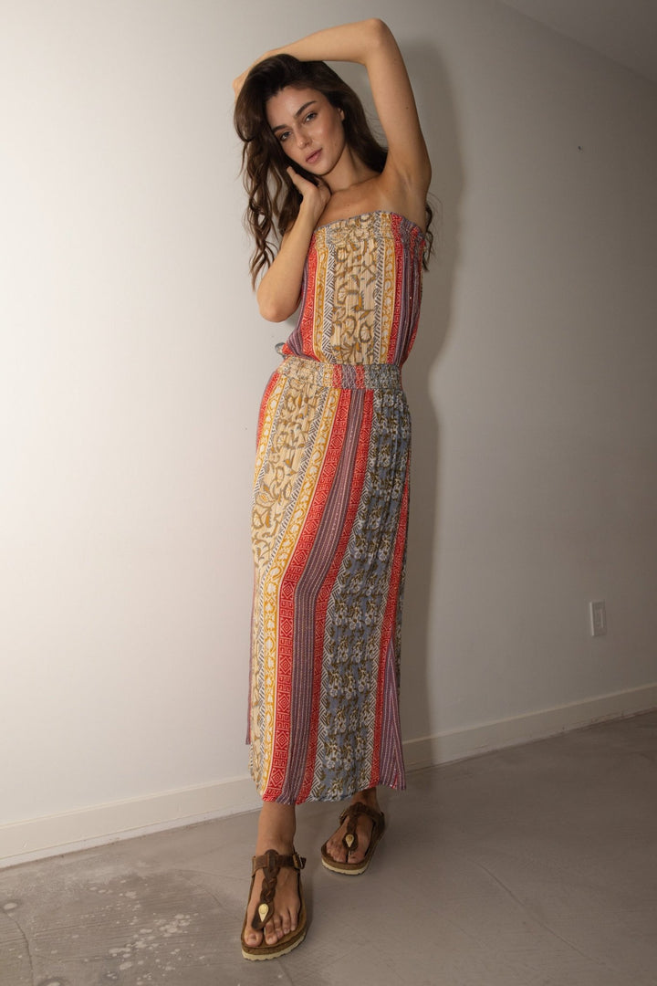 Woman wearing a patterned dress standing against a plain wall.