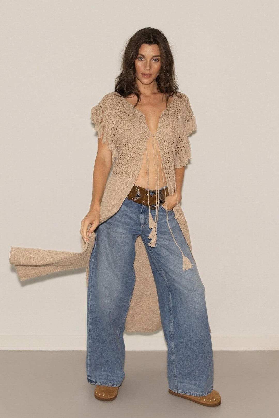 Woman wearing a beige knitted cardigan and blue jeans against a plain background