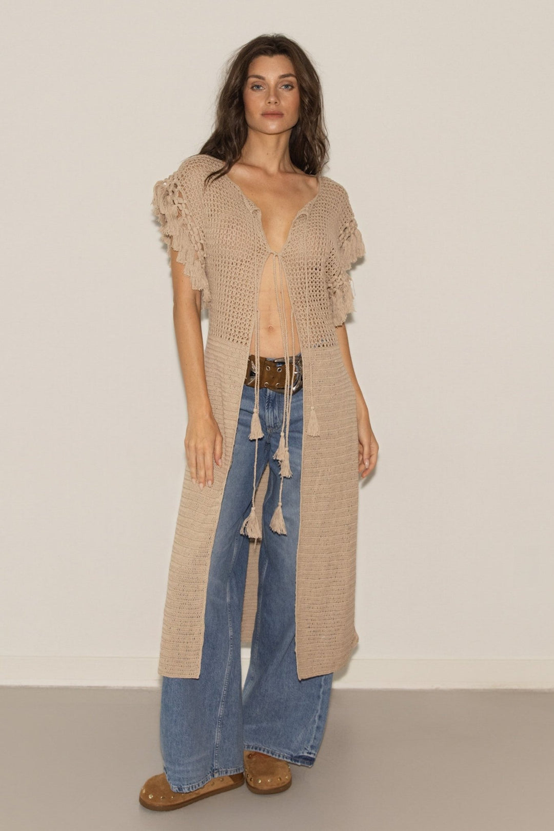 Woman wearing a long beige cardigan over a blue dress with a plain background