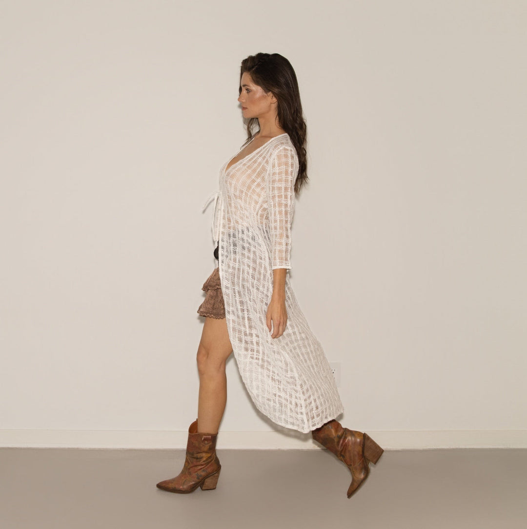 Woman walking in a white dress with a pattern and brown boots on a plain background