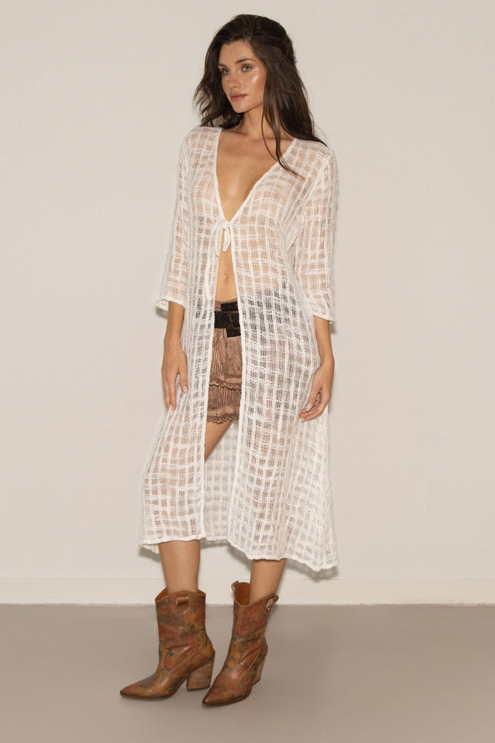 Woman wearing a long, light-colored checkered dress with brown boots on a plain background