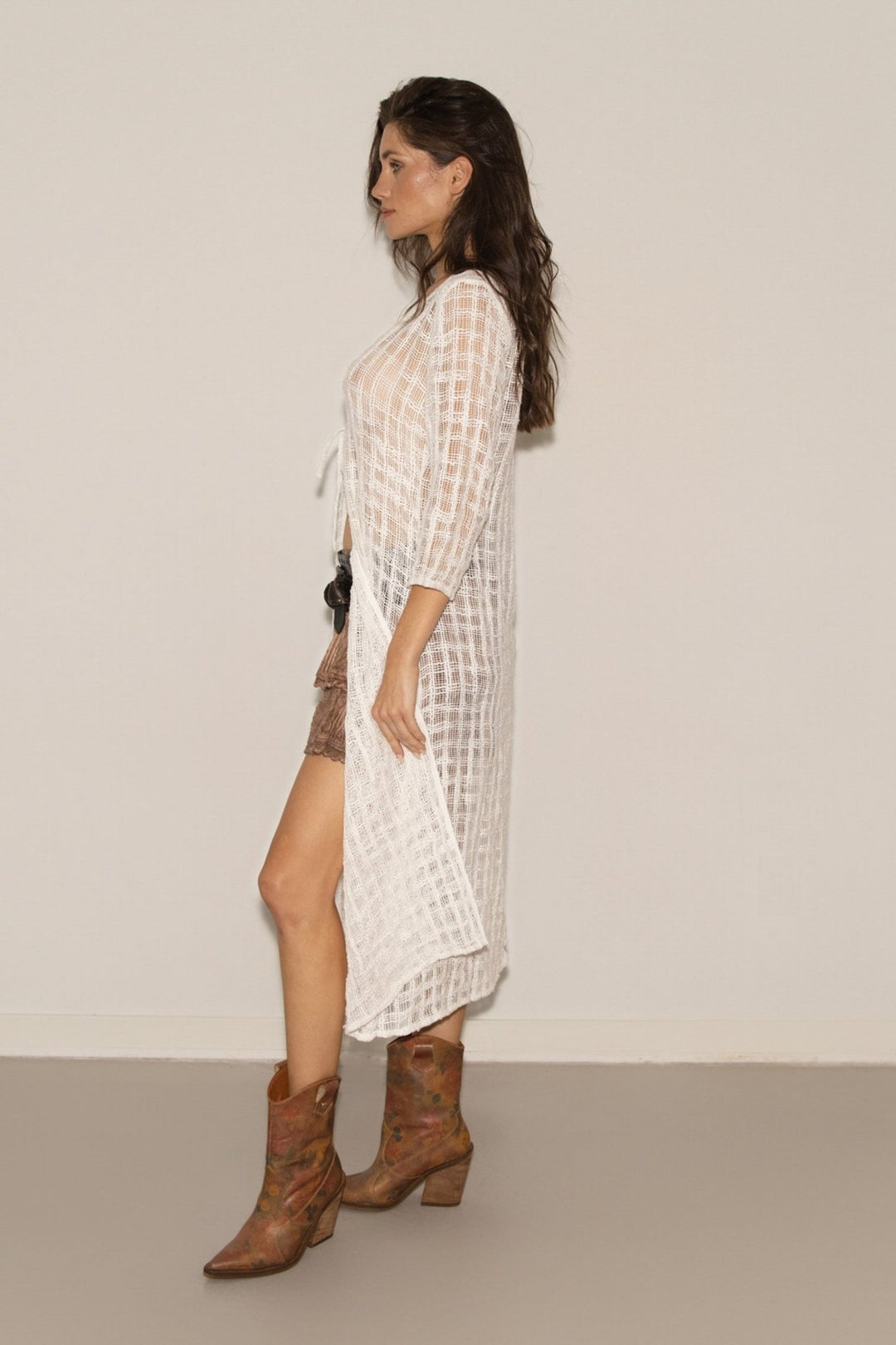 Woman wearing a white checkered dress and brown boots against a plain background