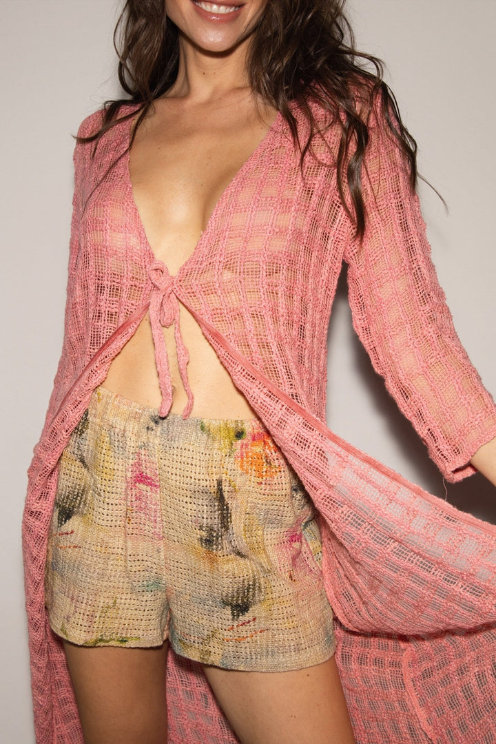 Woman wearing a pink textured cover-up and patterned shorts against a plain background