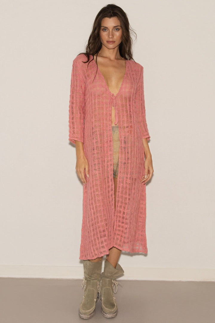 Woman wearing a pink textured cover-up over a green swimsuit with beige boots against a white background