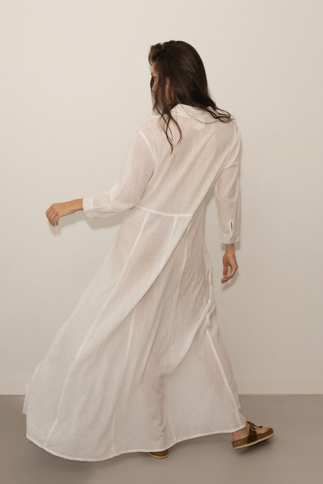 Woman wearing a long, WHITE dress against a plain background