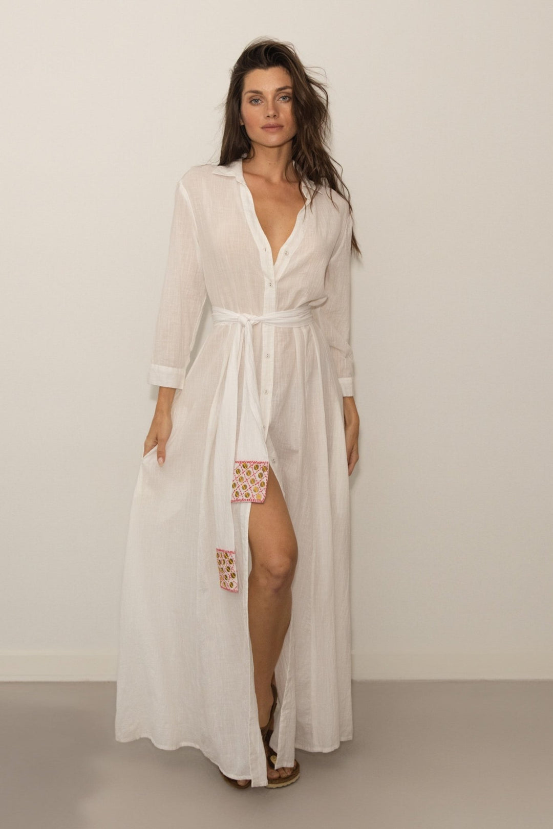 Woman wearing a long white dress with floral details on a plain background