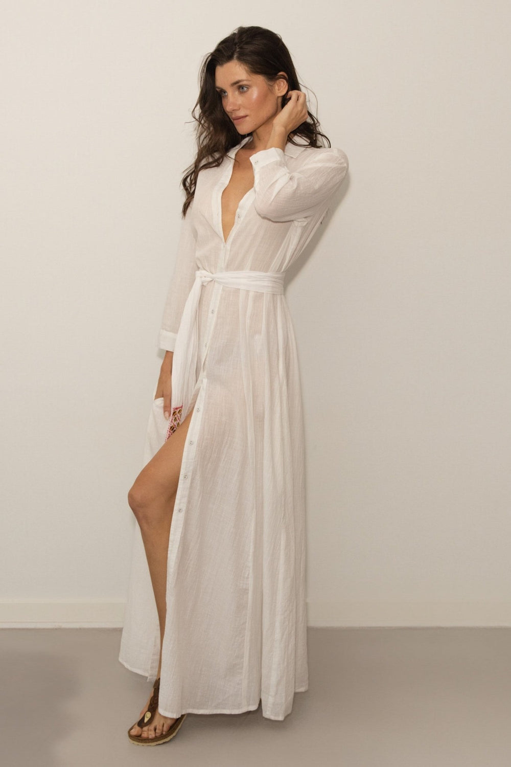 Woman wearing a white dress with a slit on a plain background