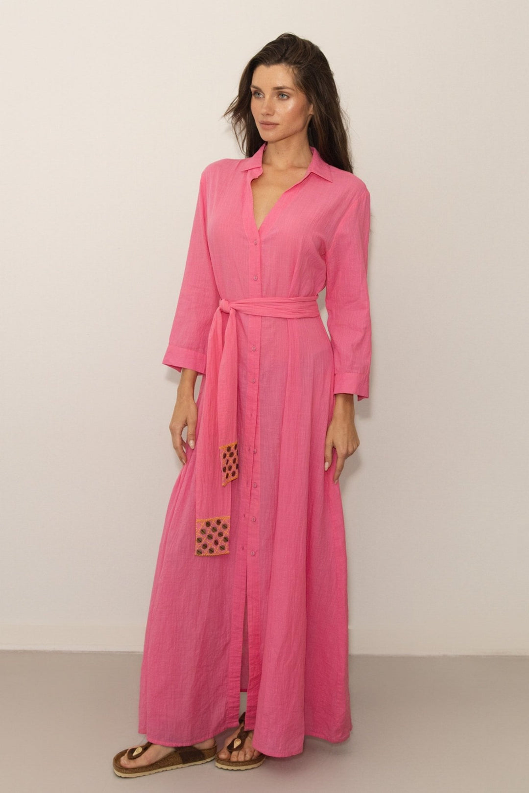 Woman wearing a pink dress with a belt against a plain background