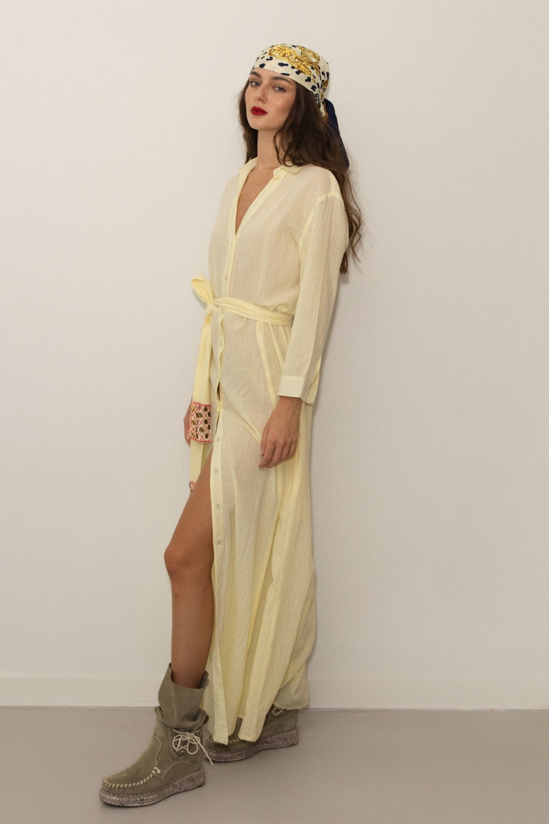 Woman wearing a light yellow dress with a headscarf against a plain background