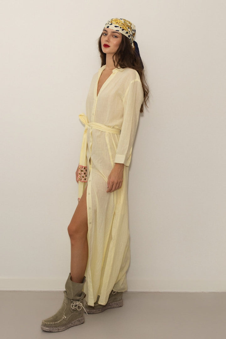 Woman wearing a light yellow dress with a headscarf against a plain background