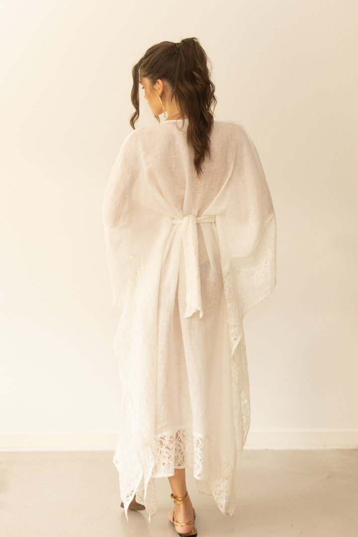 Woman wearing a light beige kimono-style garment with lace details on a plain background