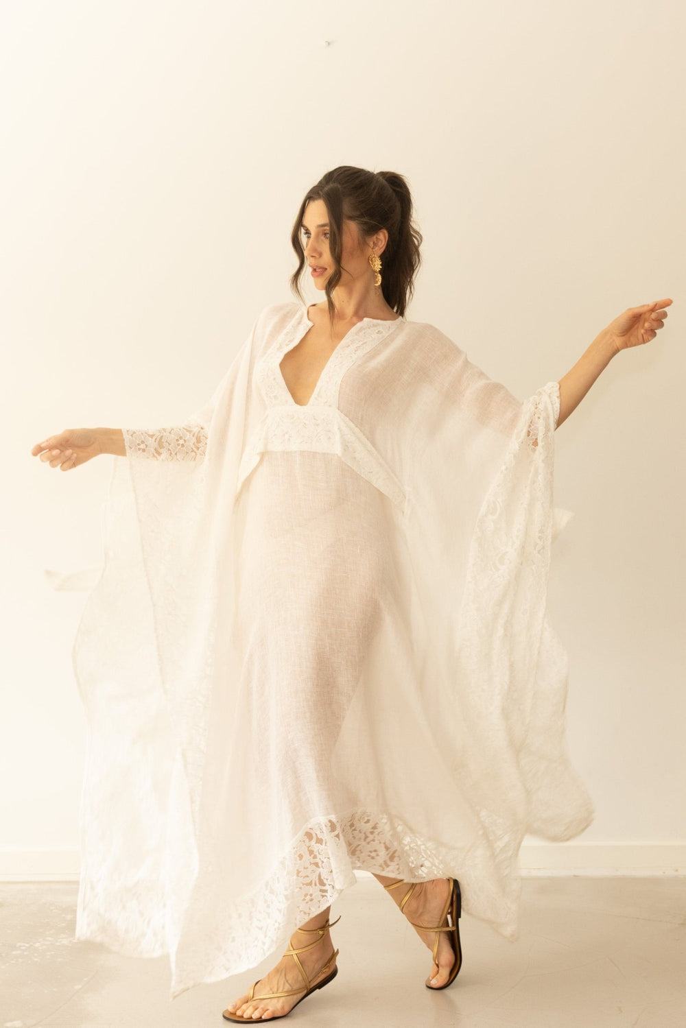 Woman wearing a flowing white dress with lace details against a plain background