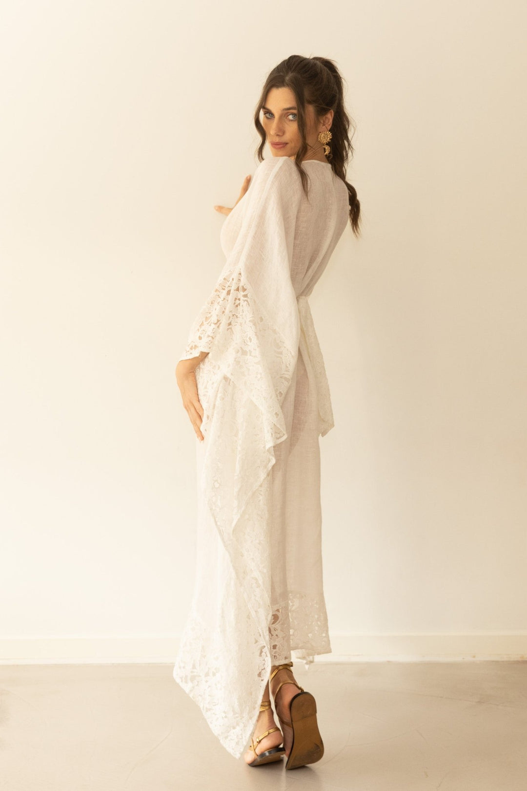 Woman wearing a long, light-colored dress with a sheer overlay against a white background