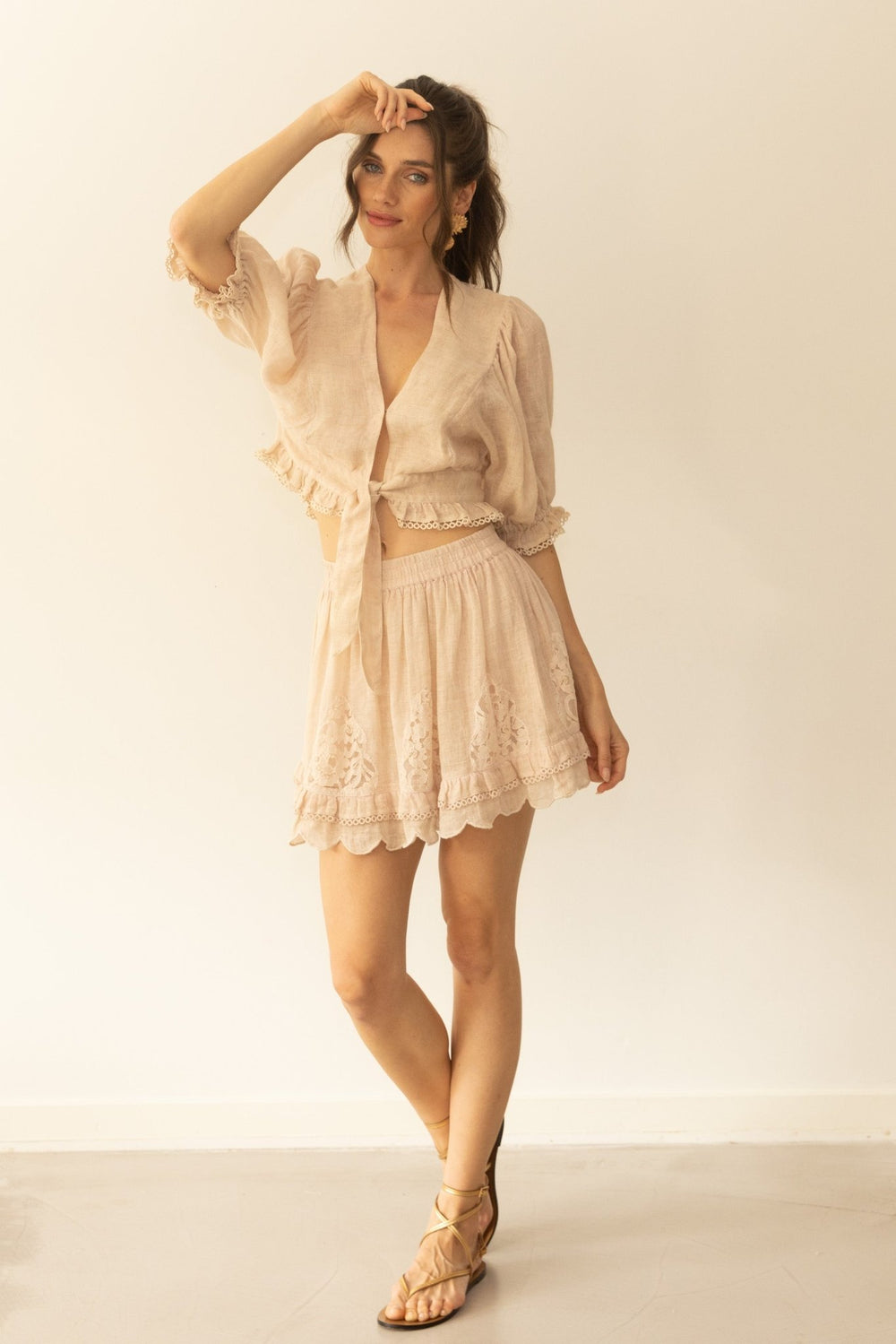 Woman wearing a beige lace outfit with a matching cardigan against a plain background