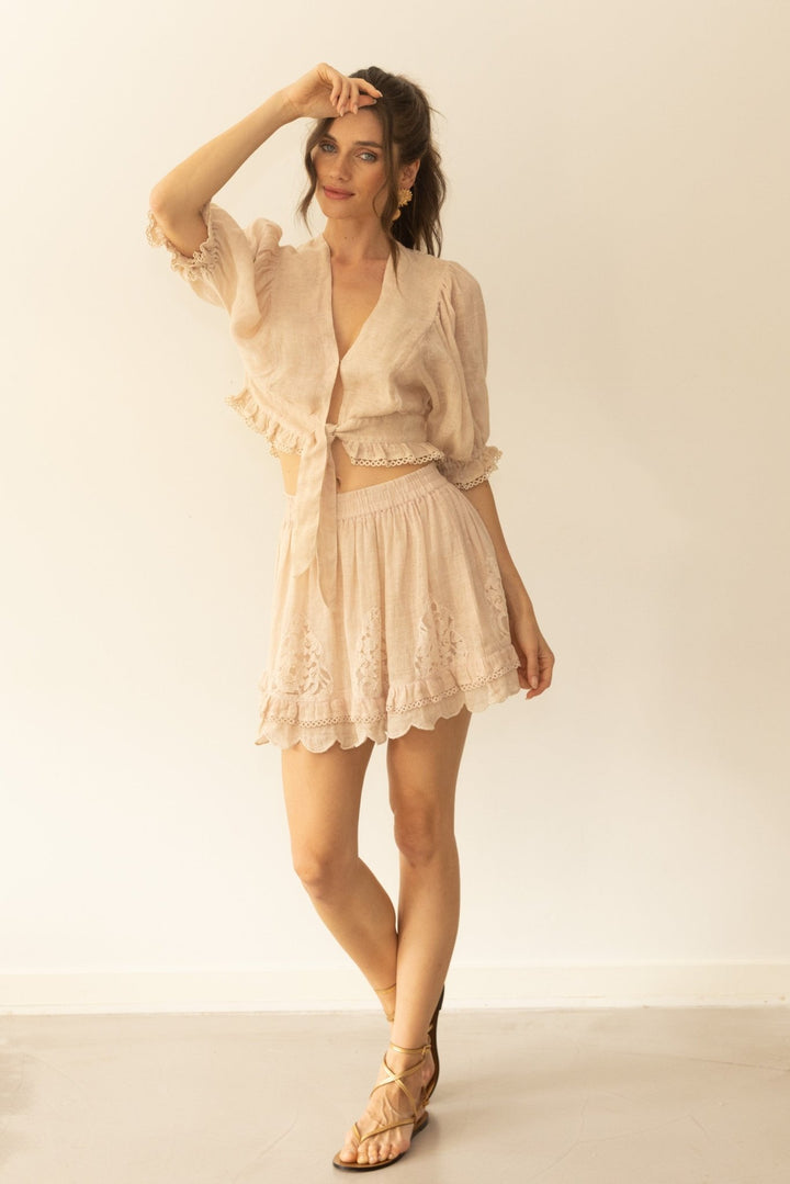 Woman wearing a beige lace outfit with a matching cardigan against a plain background