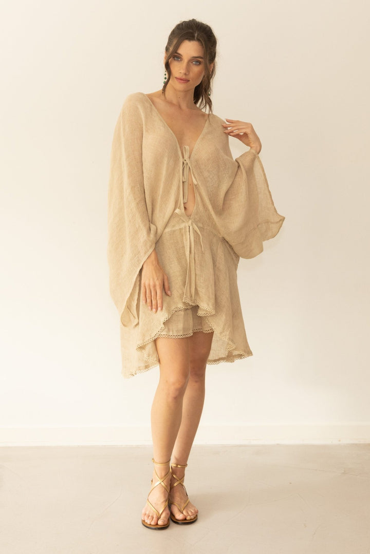 Woman wearing a beige outfit with a sheer overlay against a plain background