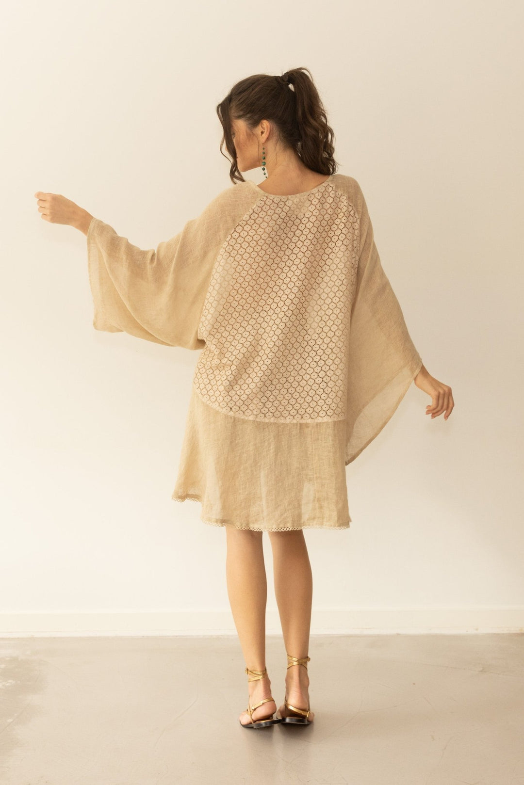 Woman wearing a beige poncho with a subtle pattern against a plain background