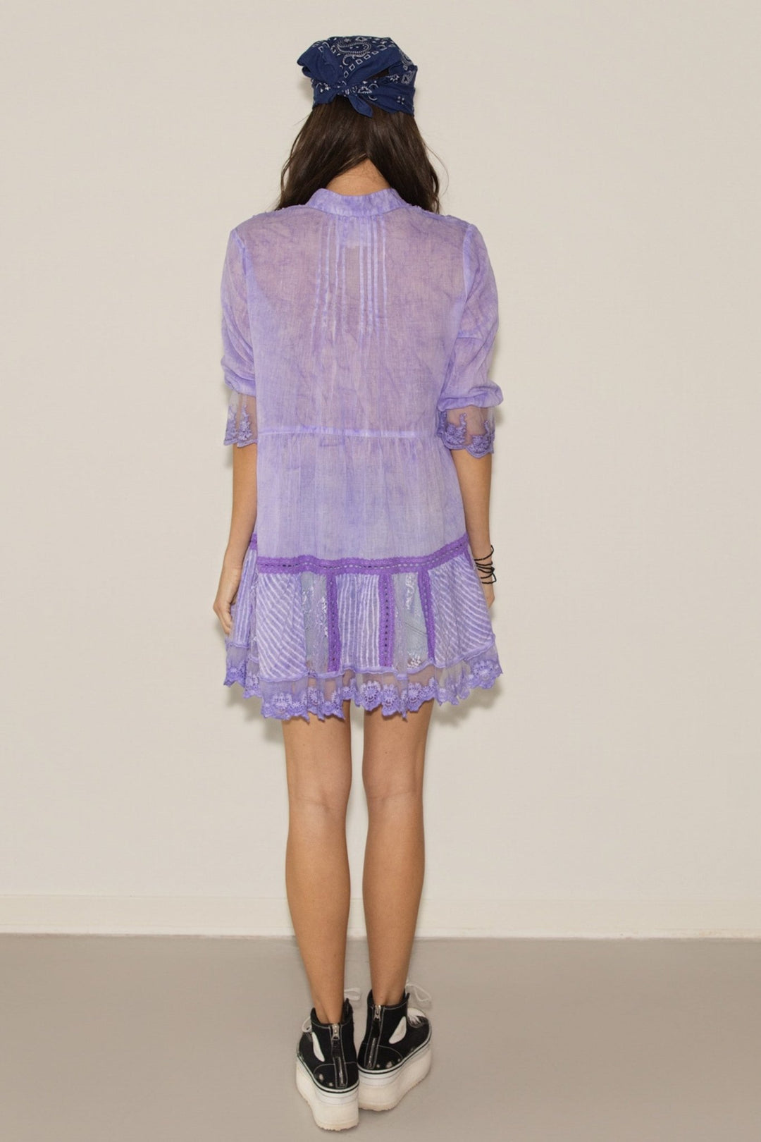 Person wearing a light purple dress with a lace overlay on a plain background