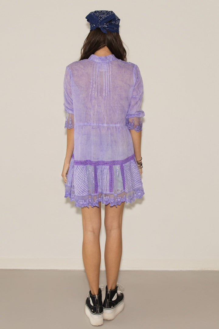 Person wearing a light purple dress with a lace overlay on a plain background