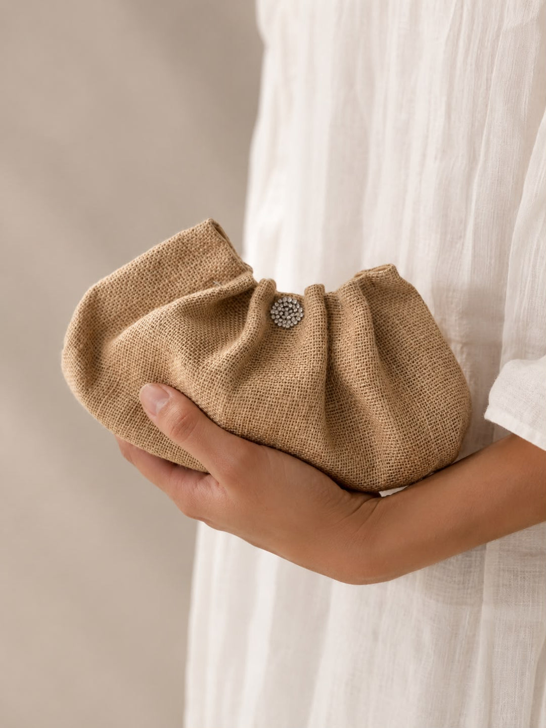 Hand holding a textured beige clutch bag with a subtle design detail against a neutral background.