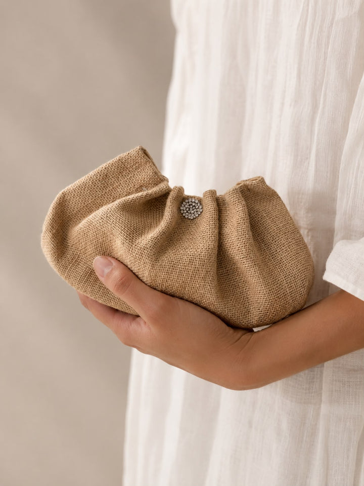 Hand holding a textured beige clutch bag with a subtle design detail against a neutral background.